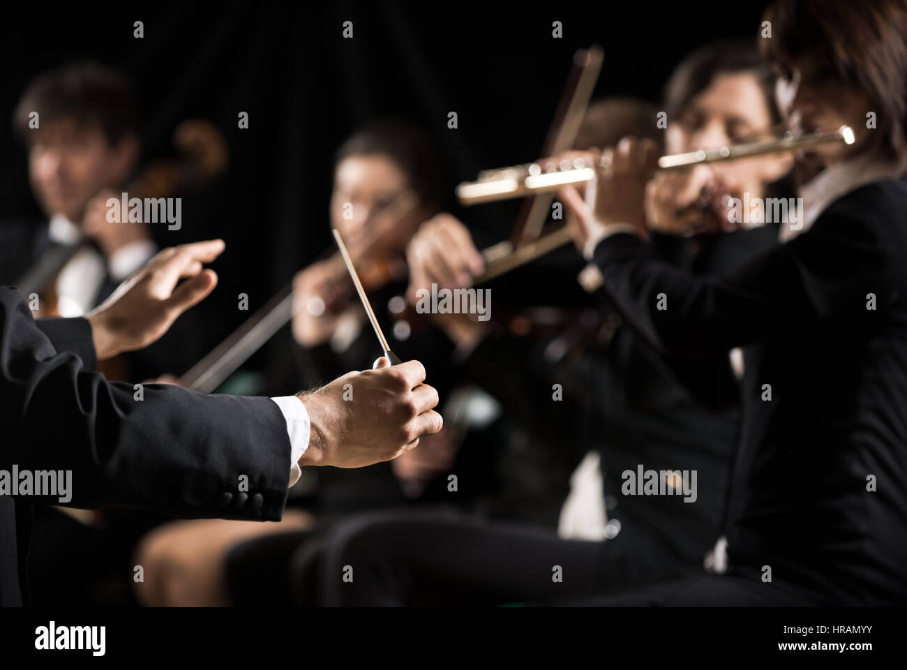Conductor directing symphony orchestra with performers on background ...