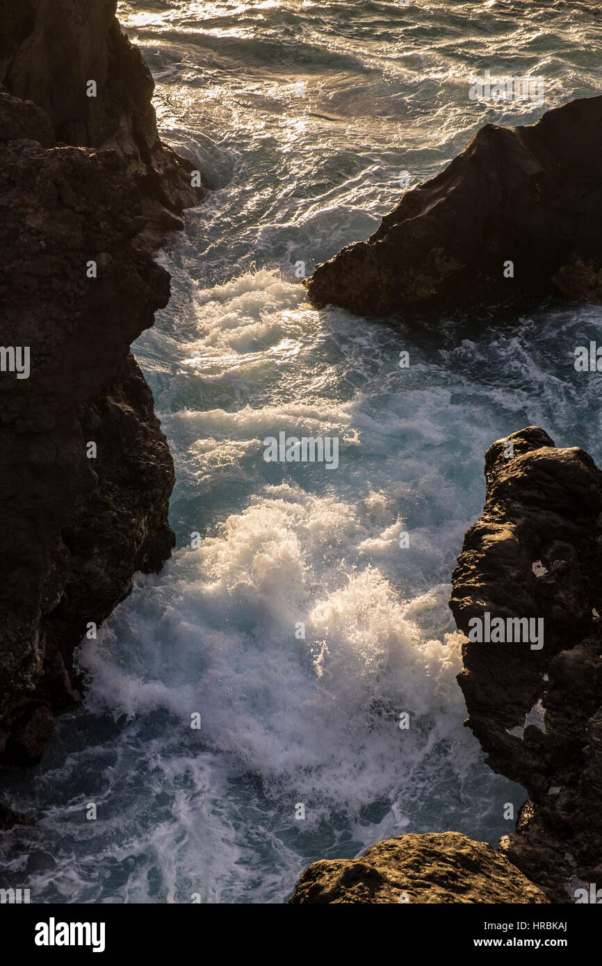 Sea rushing in between rocks in late evening light on the west coast of ...