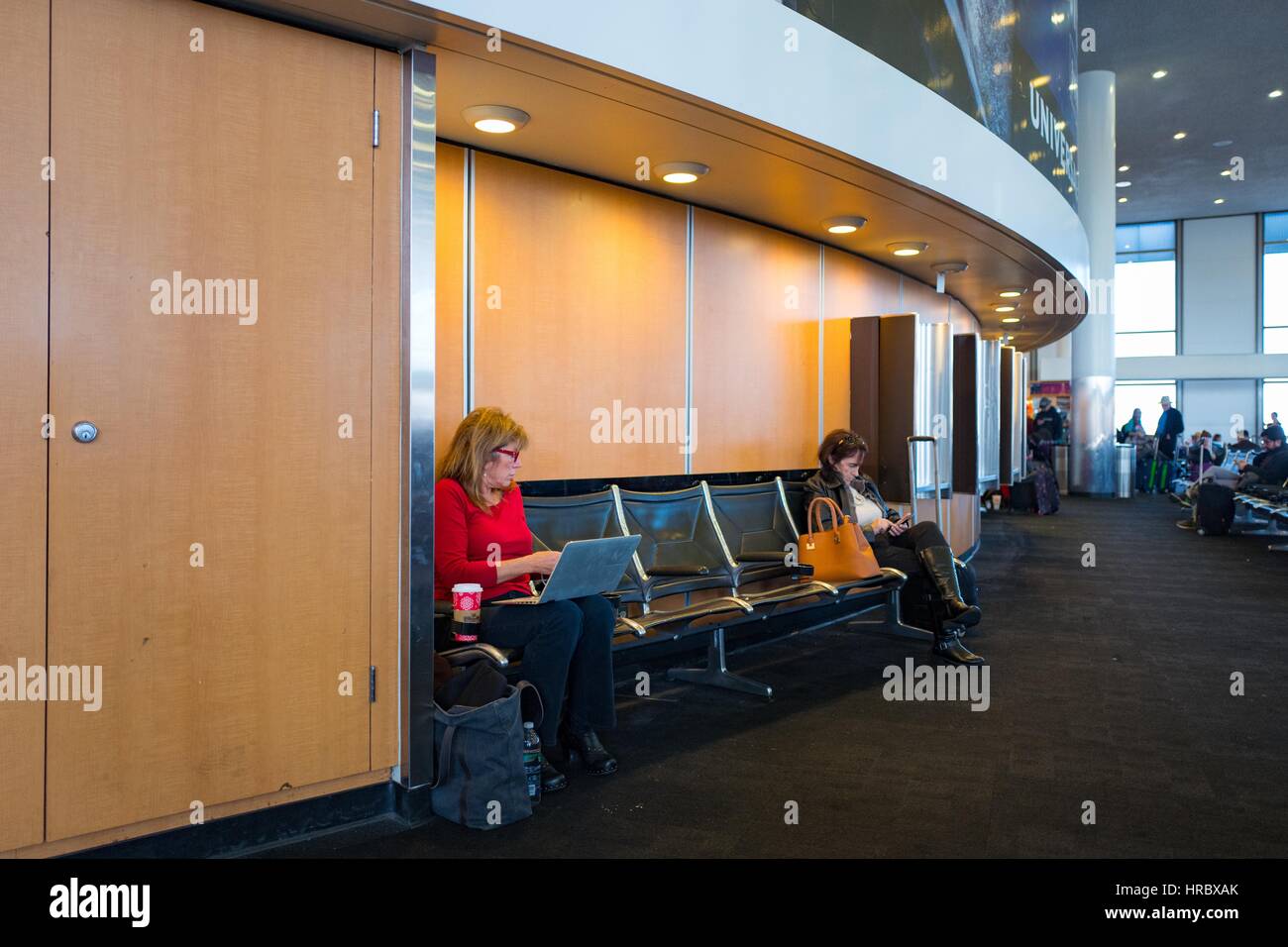 Two female travelers sit on benches and work on their laptops and