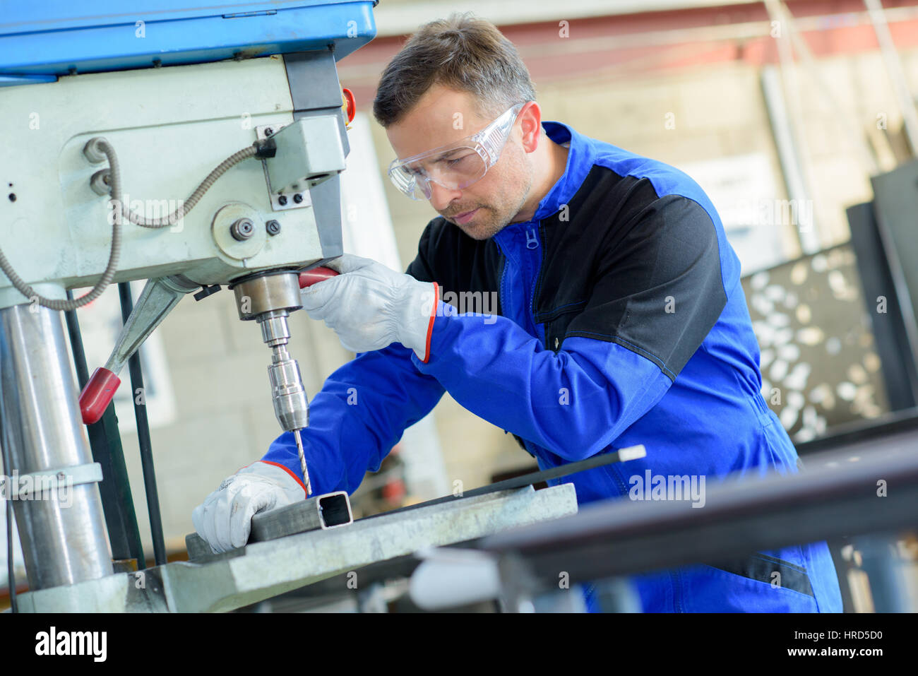 Workman drilling through square steel bar Stock Photo - Alamy