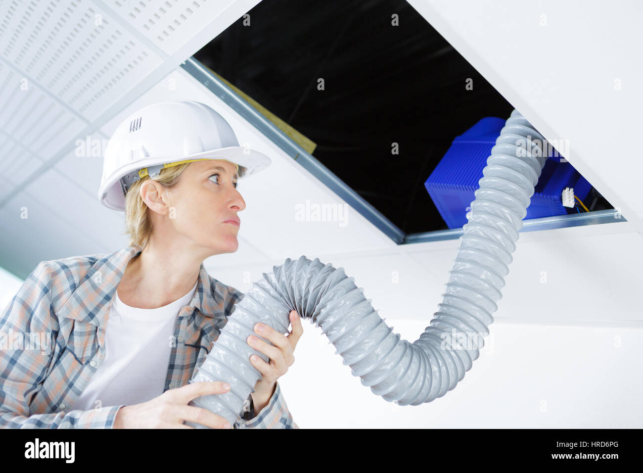 female worker fitting ventilation system in buildings ceiling Stock