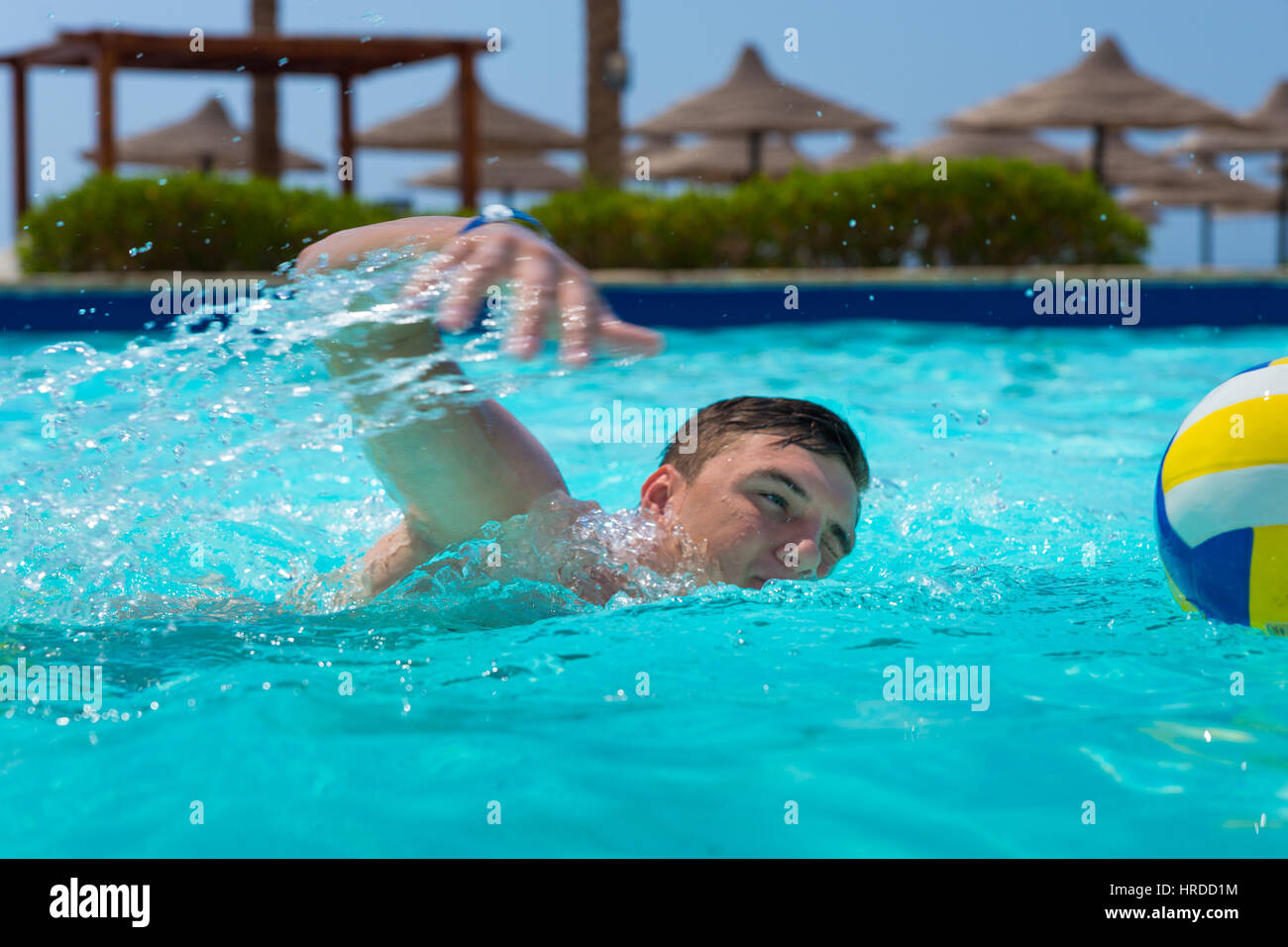 Young man swimming near ball in a pool at the hotel on a sunny summer day Stock Photo