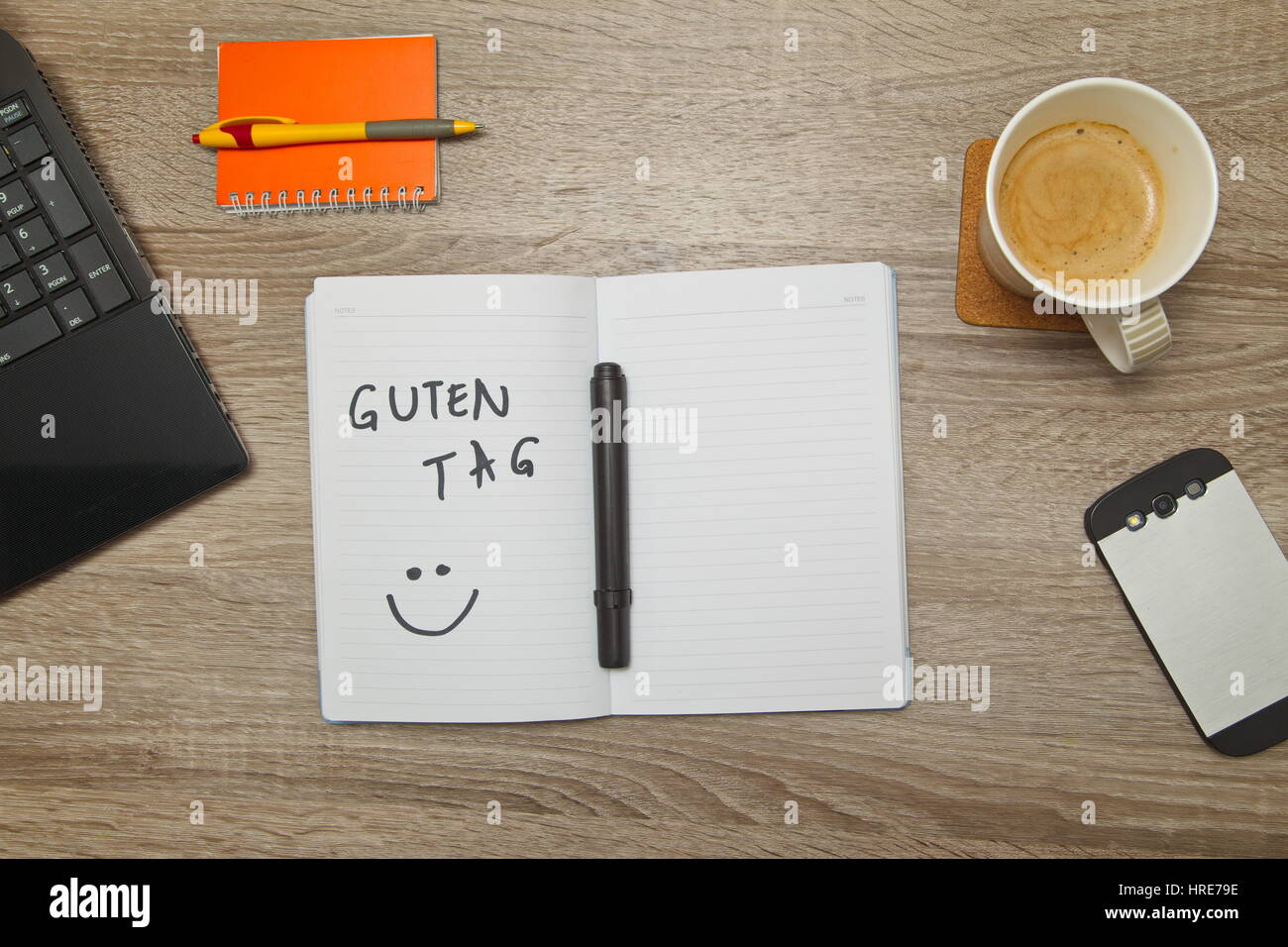 Open notebook with German text 'GUTEN TAG' (Good afternoon)  and a cup of coffee on wooden background. Top down view Stock Photo