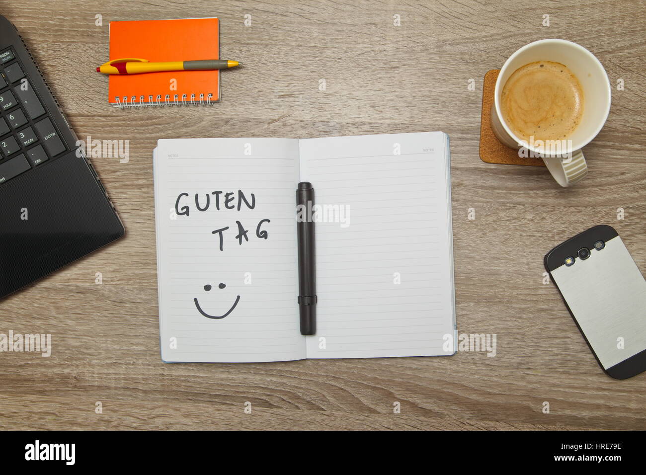 Open notebook with German text "GUTEN TAG" (Good afternoon) and a cup of coffee on wooden