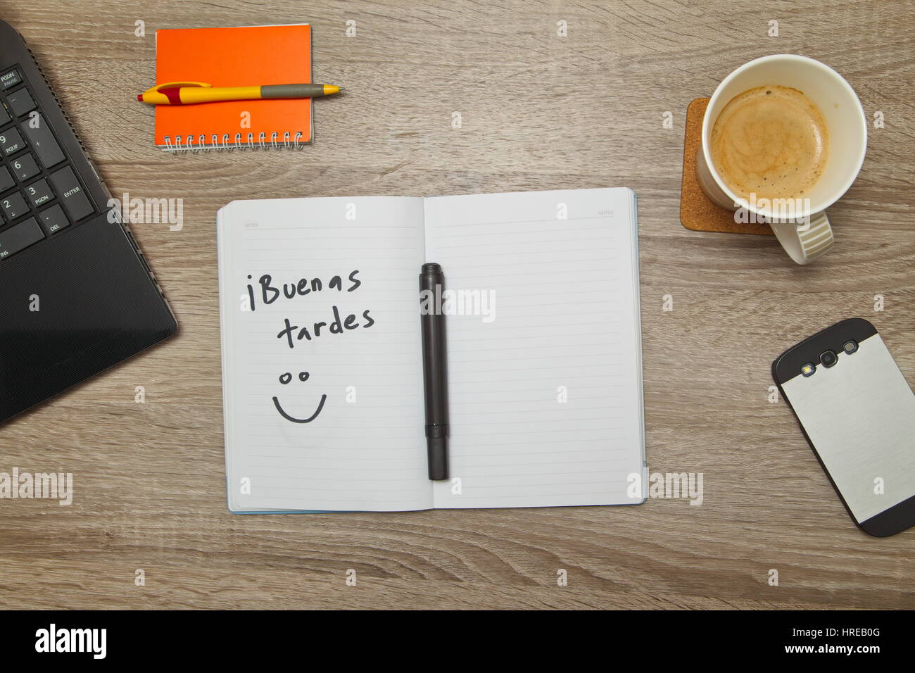 Open notebook with Spanish words 'Buenas Tardes' ( Good Afternoon) and a cup of coffee on wooden background. Stock Photo