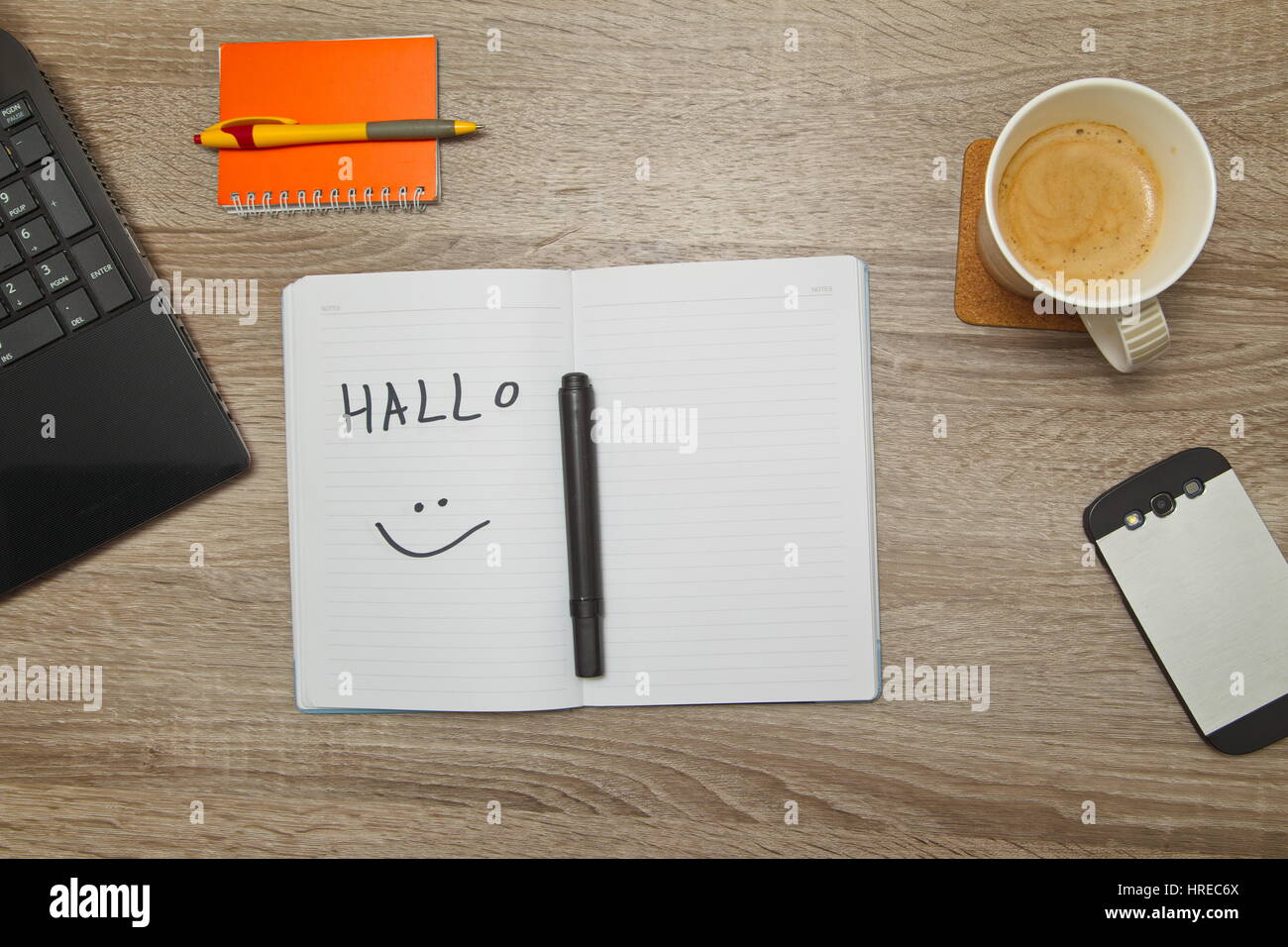 Open notebook with German word 'HALLO' ( Hello) and a cup of coffee on wooden background. Top down view Stock Photo