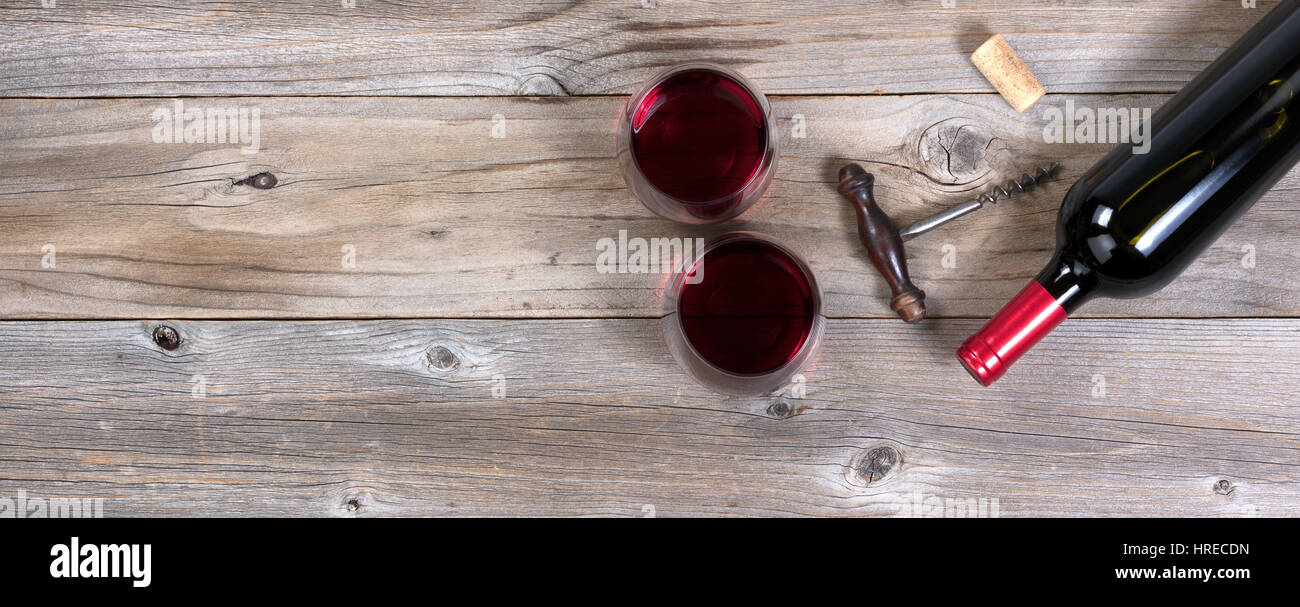 Flat view of a bottle of red wine, antique corkscrew, and full drinking glasses on rustic wooden boards Stock Photo