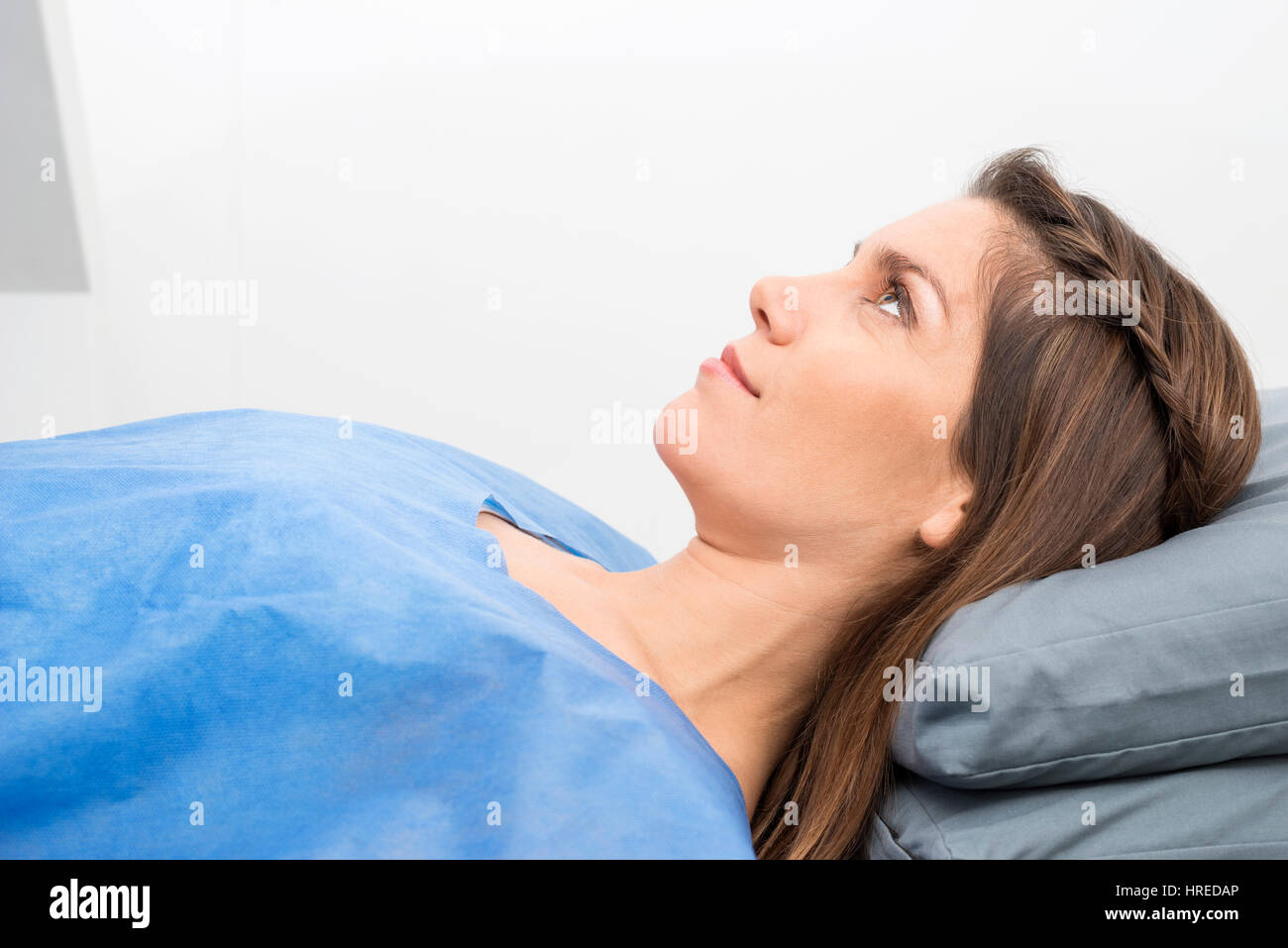 Side view of mid adult female patient in protective clothing lying on bed in examination room Stock Photo