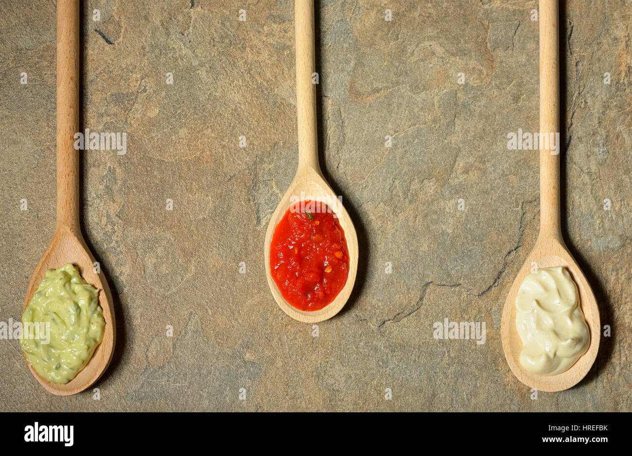 different types of sauces in spoons on stone table Stock Photo