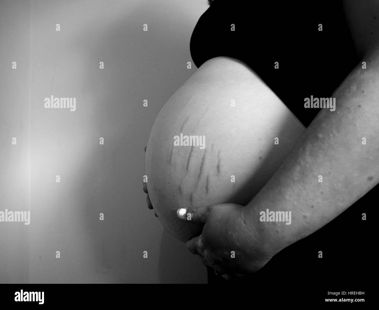 A heavily pregnant belly, with several stretchmarks, is cradled by the mothers hands. Stock Photo