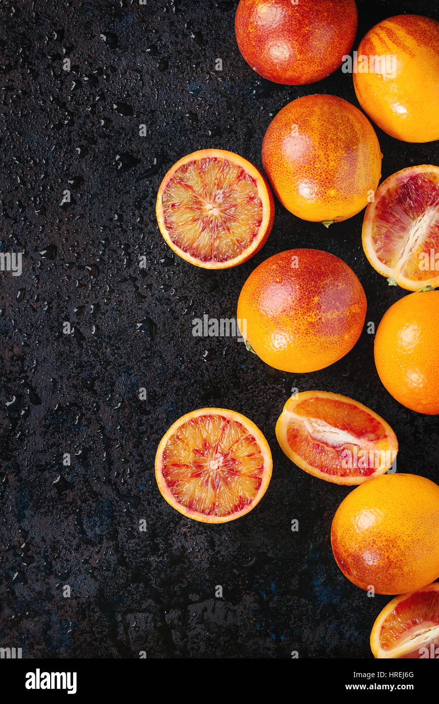 Sliced and whole ripe juicy Sicilian Blood oranges fruits on black wet metal texture background. Top view with space Stock Photo