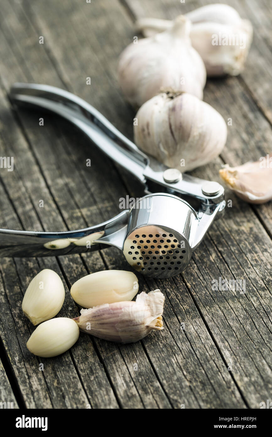 Garlic and garlic press on old wooden table. Stock Photo