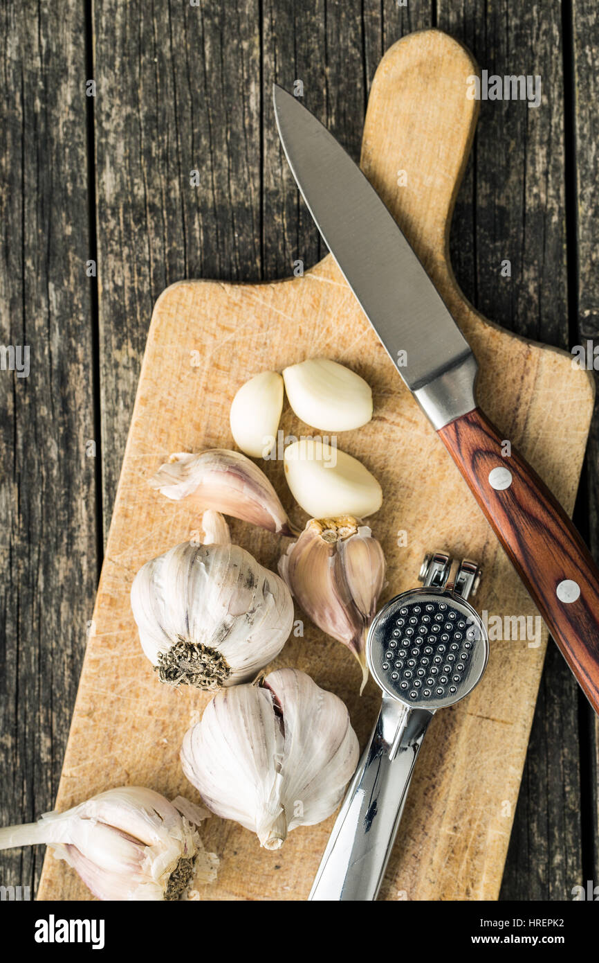 Garlic and garlic press on cutting board and knife. Top view. Stock Photo