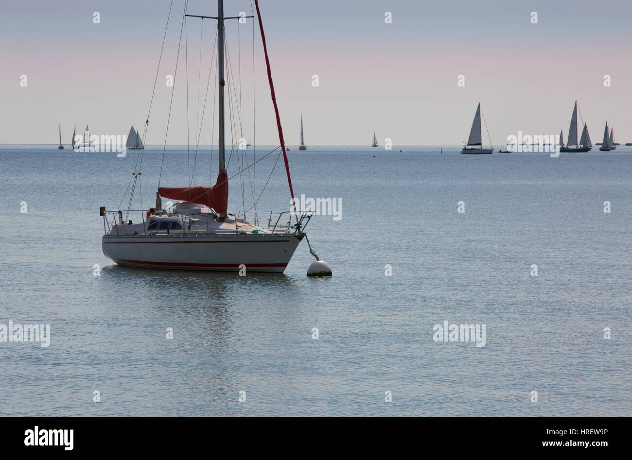 A sailing boat at its moorings with a yacht race in progress in the distance Stock Photo