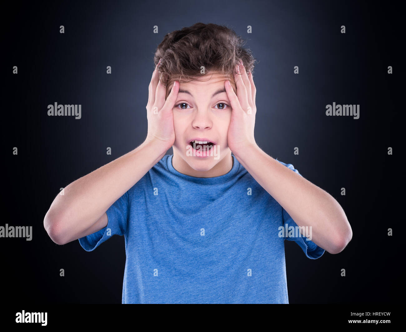 Emotional portrait of caucasian teen boy. Amazed teenager screaming looking at camera. Handsome surprised child, on black background. Stock Photo