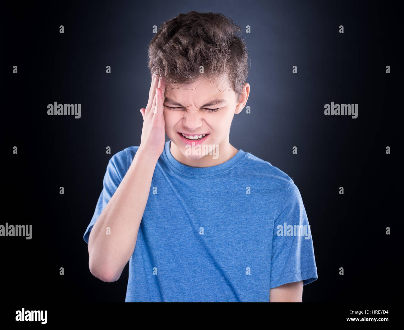 Stress and headache - teen boy having migraine pain. Handsome child suffering from a headache. Unhappy caucasian teenager touching his head, with eyes Stock Photo