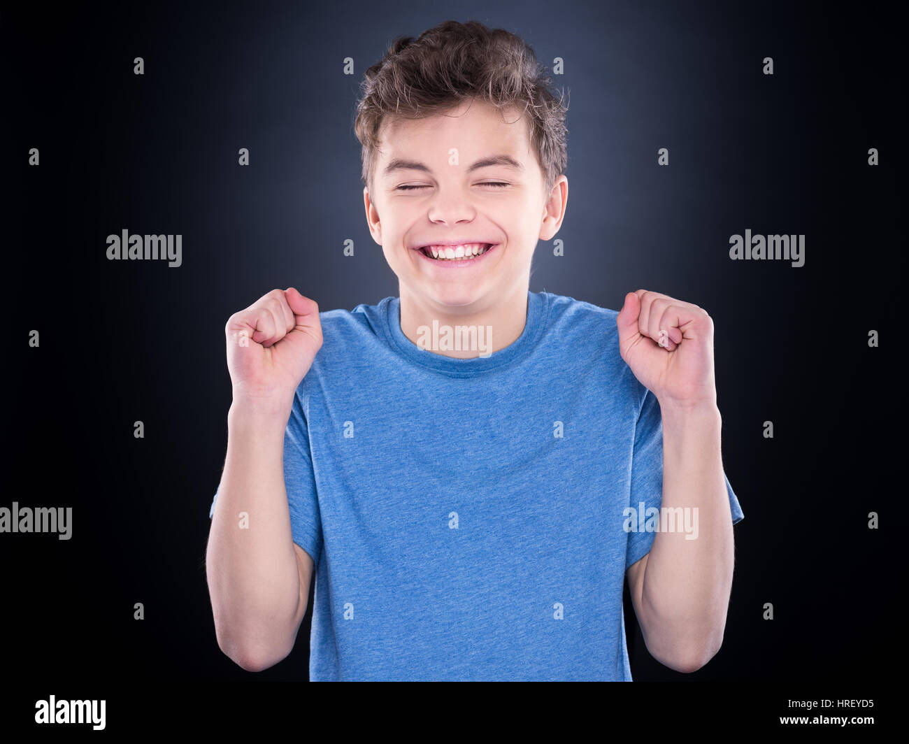 Half-length emotional portrait of caucasian teen boy. Victory screaming teenager wearing blue t-shirt on black background. Funny winner child shouting Stock Photo