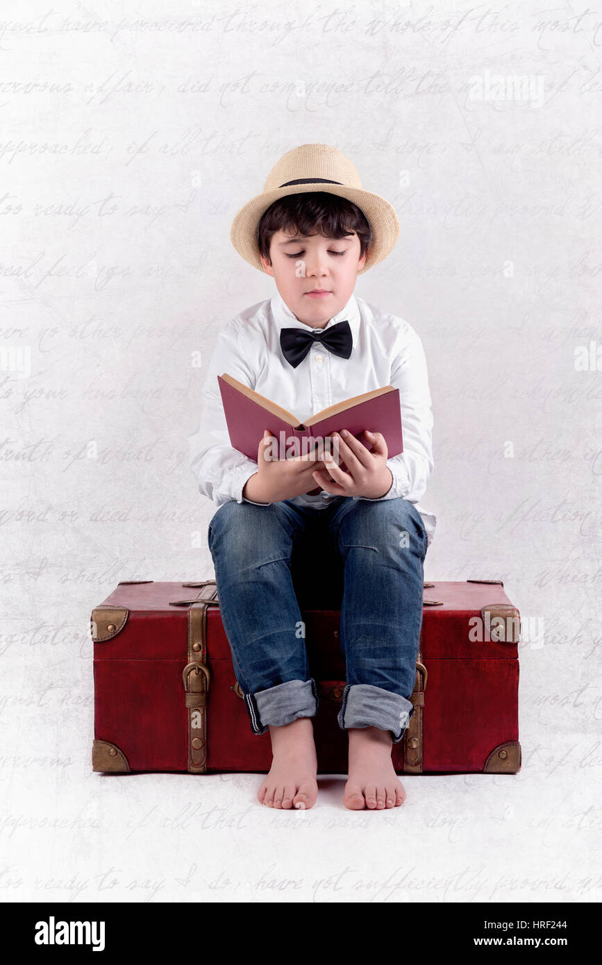 Boy reading a book sitting in a suitcase. Composite image of boy read a