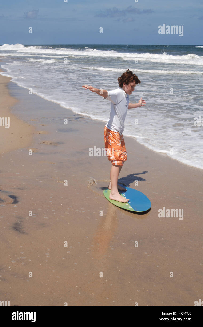 Boy child riding skim board in ocean surf on summer vacation Stock