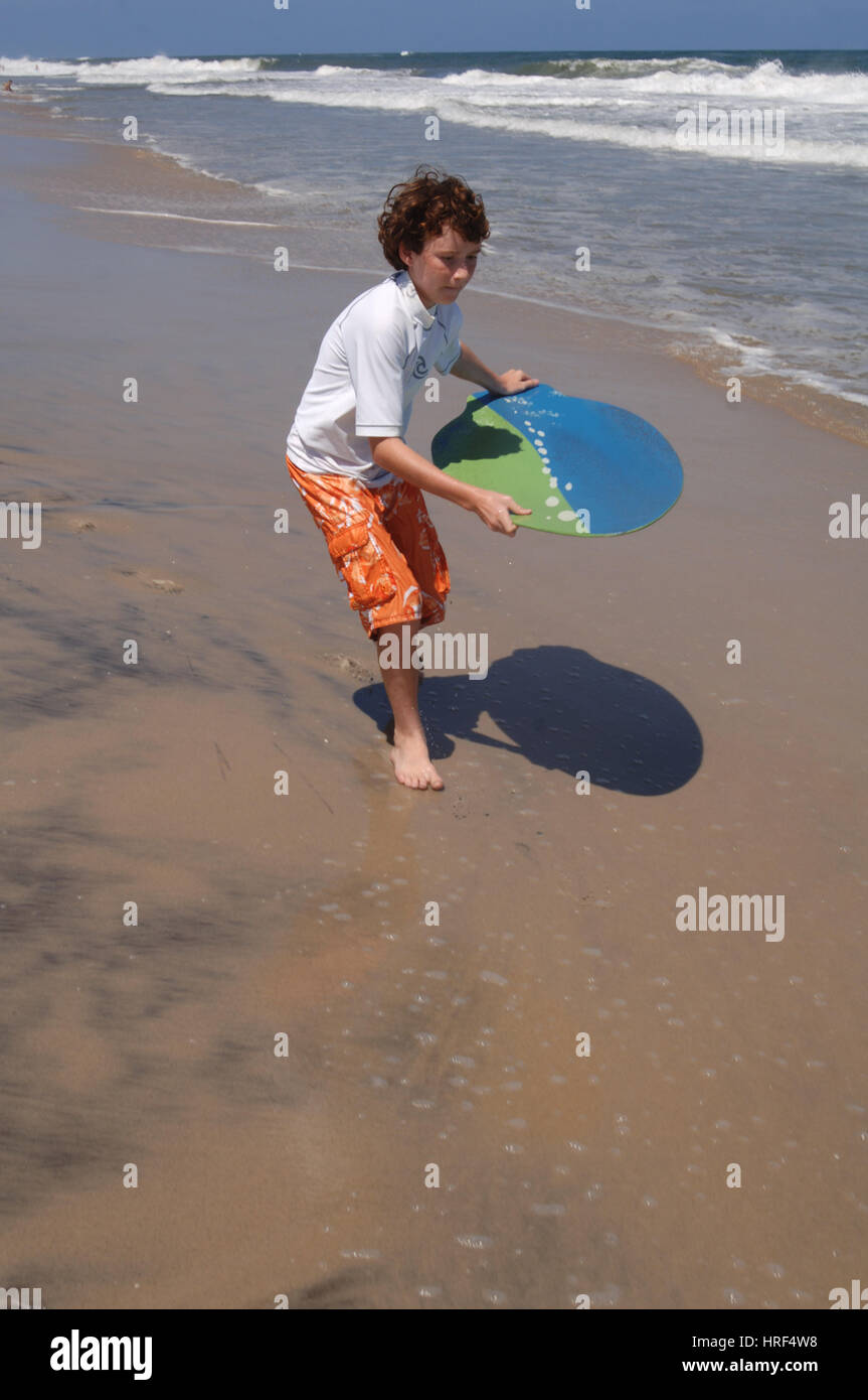 Boy child riding skim board in ocean surf on summer vacation Stock