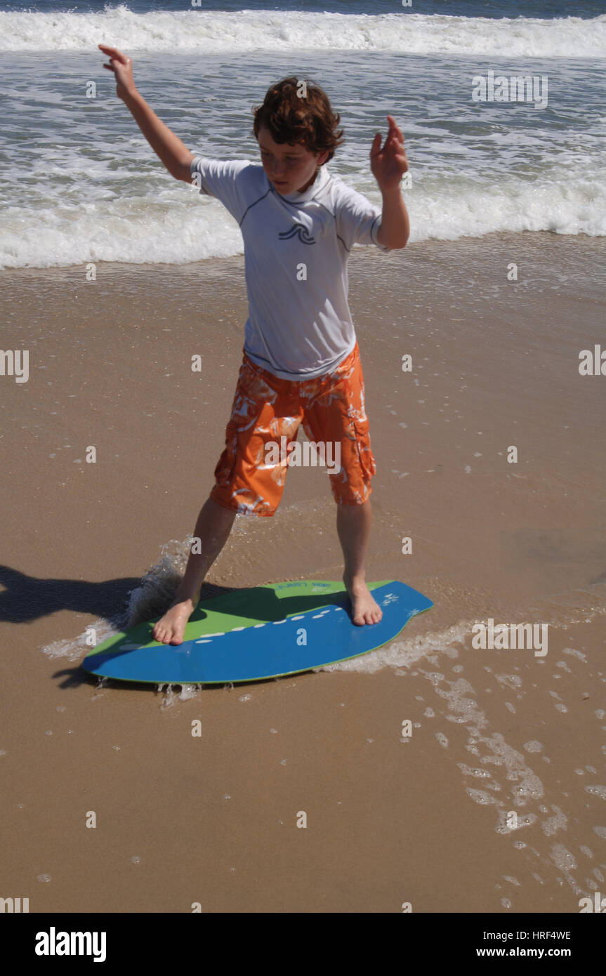 Boy child riding skim board in ocean surf on summer vacation Stock