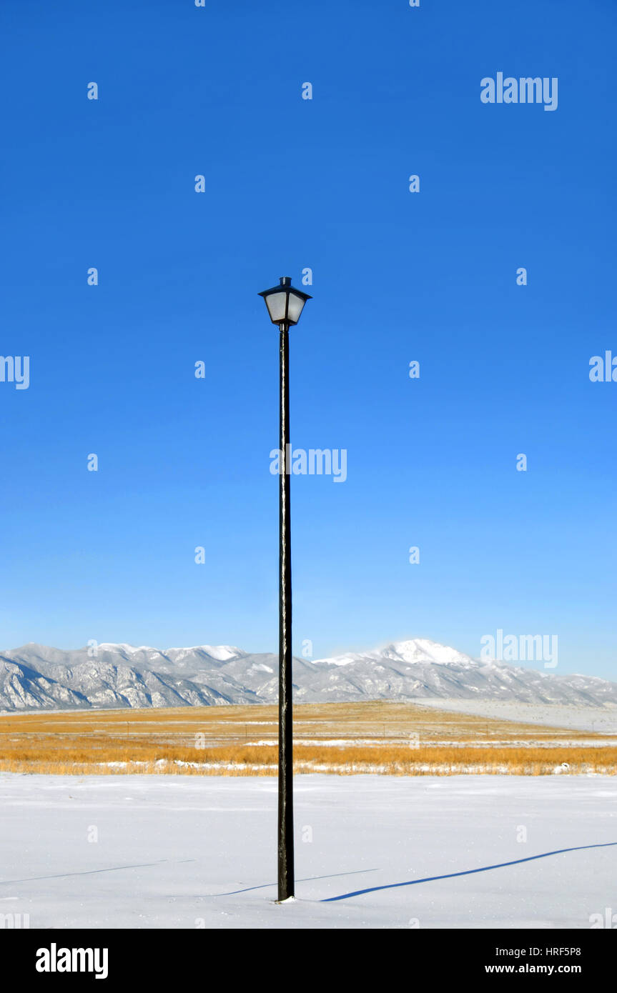 Extremely tall street light serves as night security in Colorado Springs.  Lamp tops black, iron pole.  Pole fronts Pike's Peak and the Rocky Mountain Stock Photo