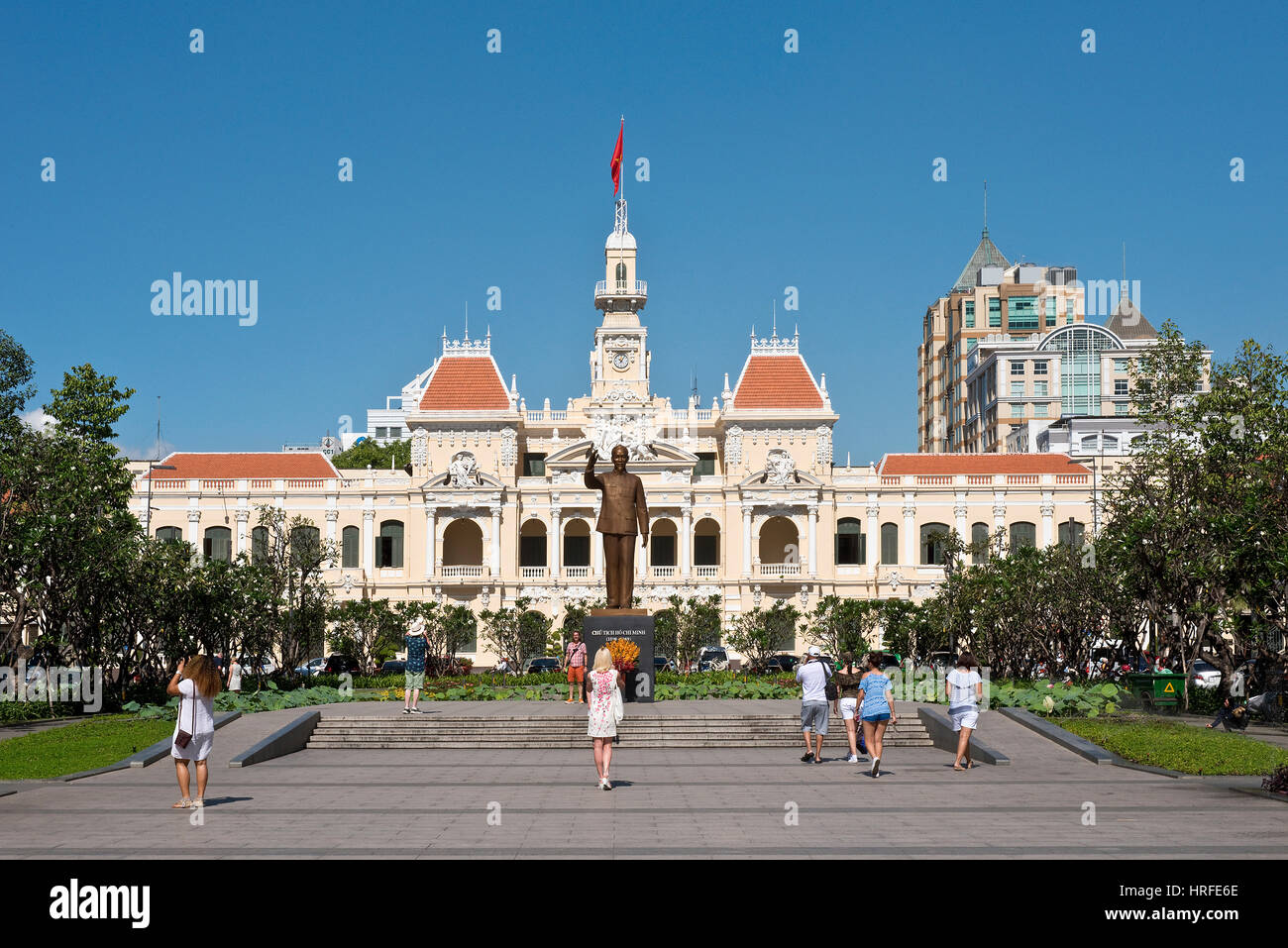 The bronze statue of Ho Chi Minh that stands outside the Ho Chi Minh City Hall on a sunny day with blue sky and tourists taking pictures. Stock Photo
