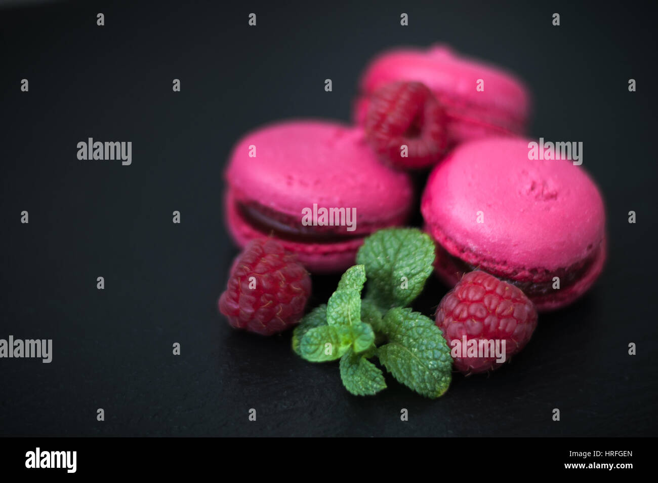 pink macaroons with raspberries on black background Stock Photo - Alamy