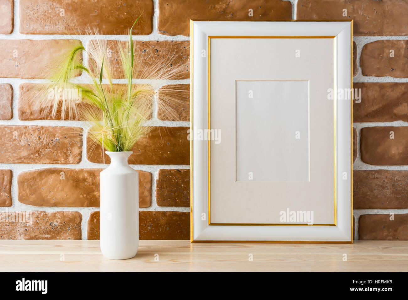 Gold decorated frame mockup with ornamental grass in styled vase near exposed brick wall. Empty frame mock up for presentation design.  Template frami Stock Photo