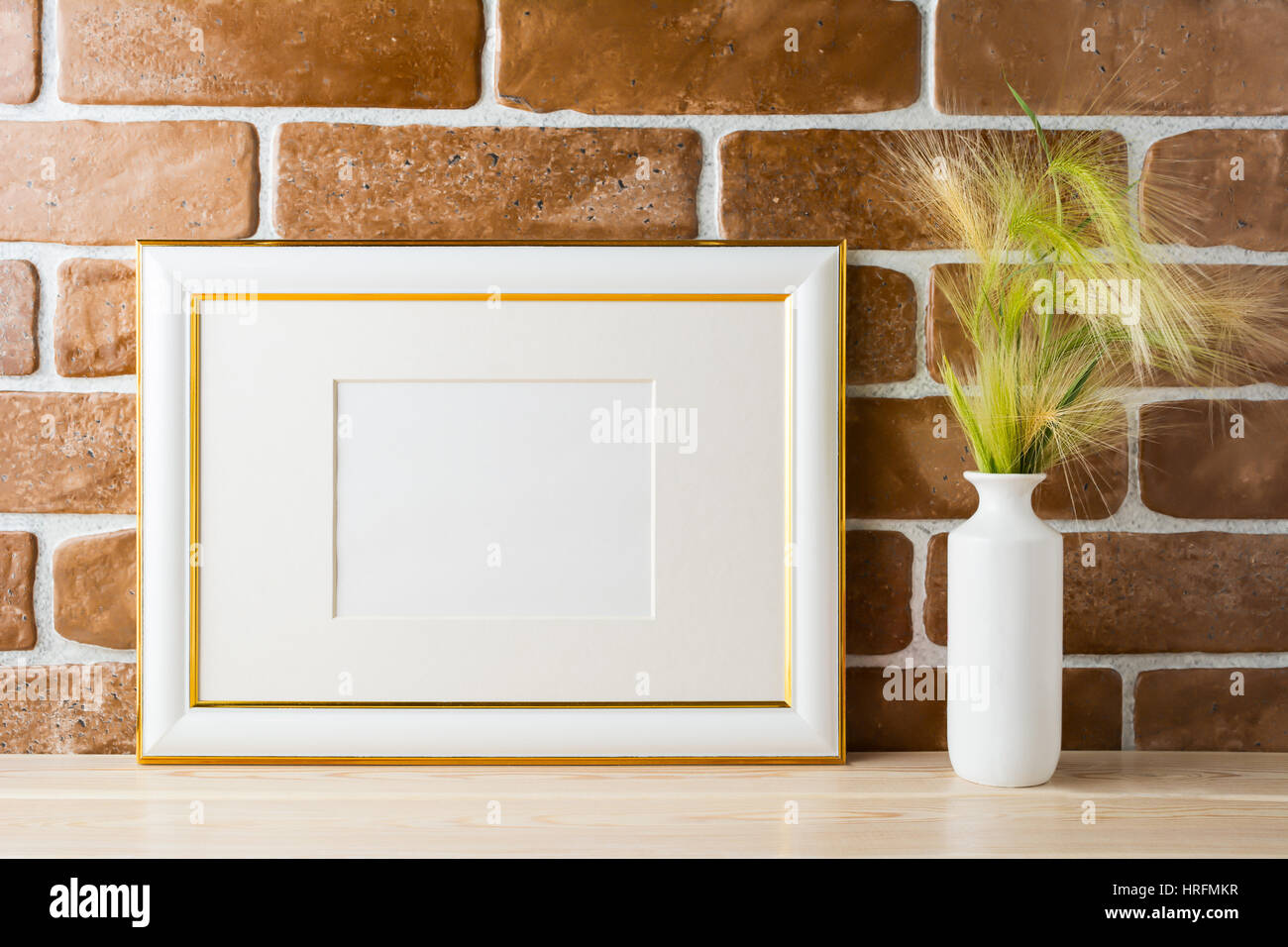 Gold decorated landscape frame mockup with ornamental grass in styled vase near exposed brick wall. Empty frame mock up for presentation design.  Temp Stock Photo