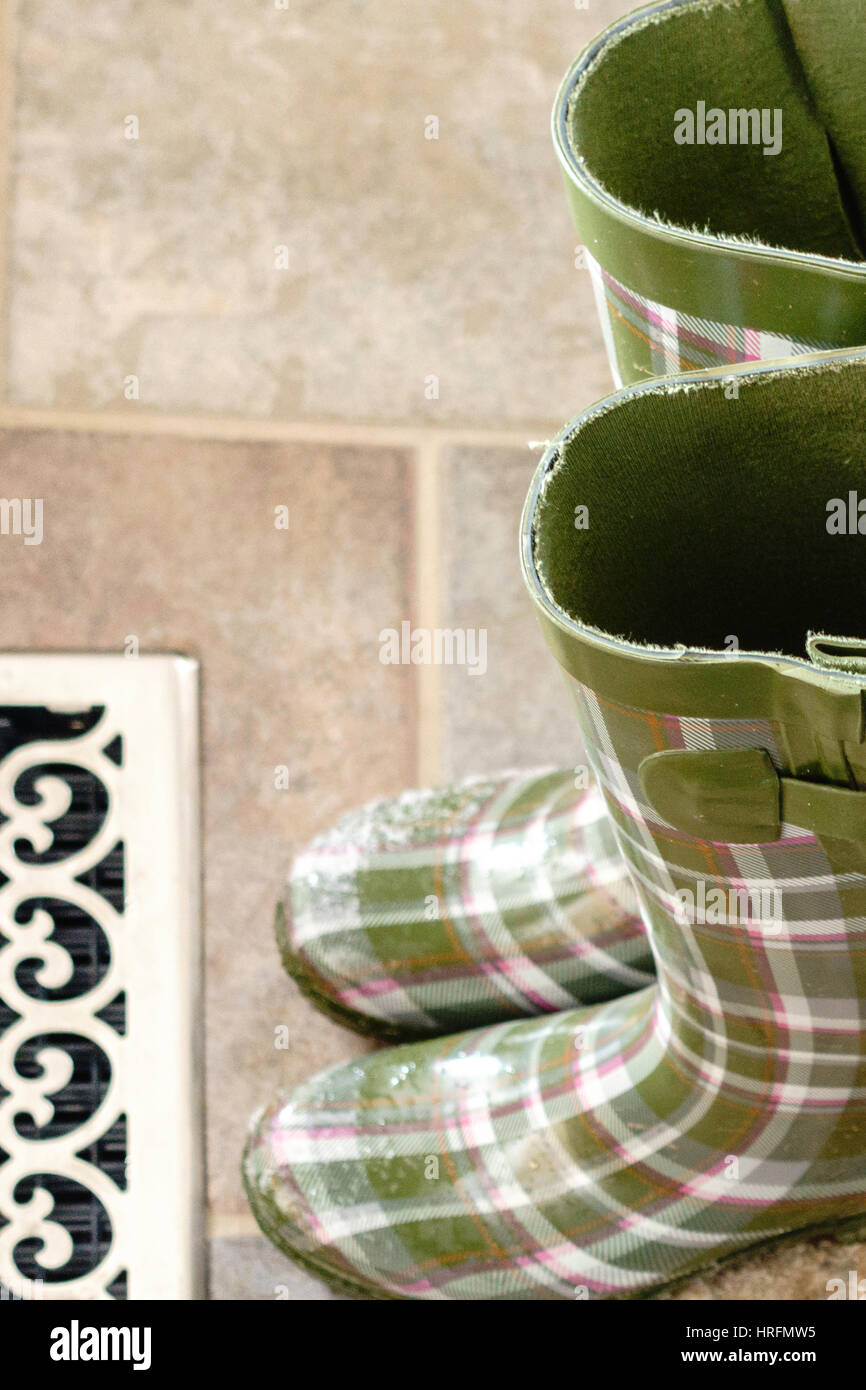 Patterned green women's rubber boots, or Wellies, with snow on the toes warming up at a floor vent indoors. Stock Photo