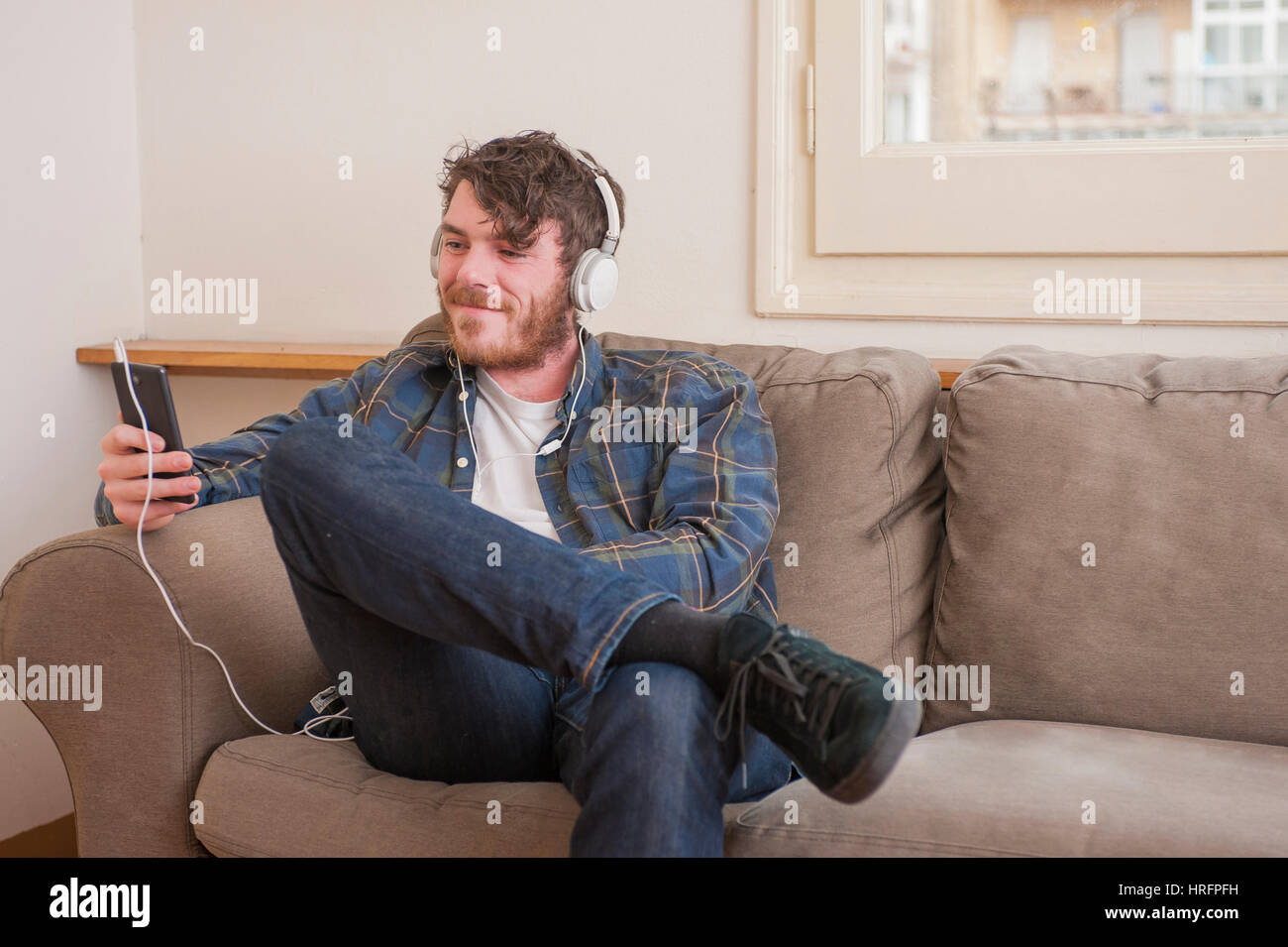 Young man at his living room with a plaid shirt listening to music Stock Photo