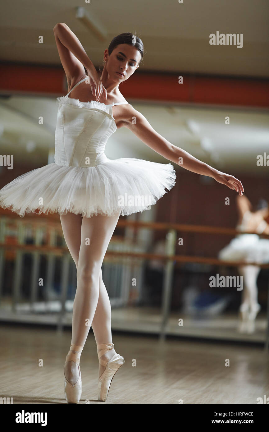 Portrait of graceful ballerina wearing white tutu dancing in half-lit ballet  studio practicing for stage performance Stock Photo - Alamy