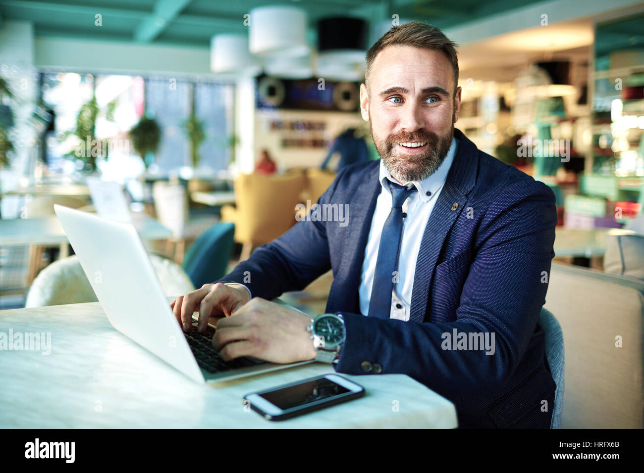 Portrait of successful mature businessman smiling and  working at laptop in modern lounge of restaurants lounge Stock Photo