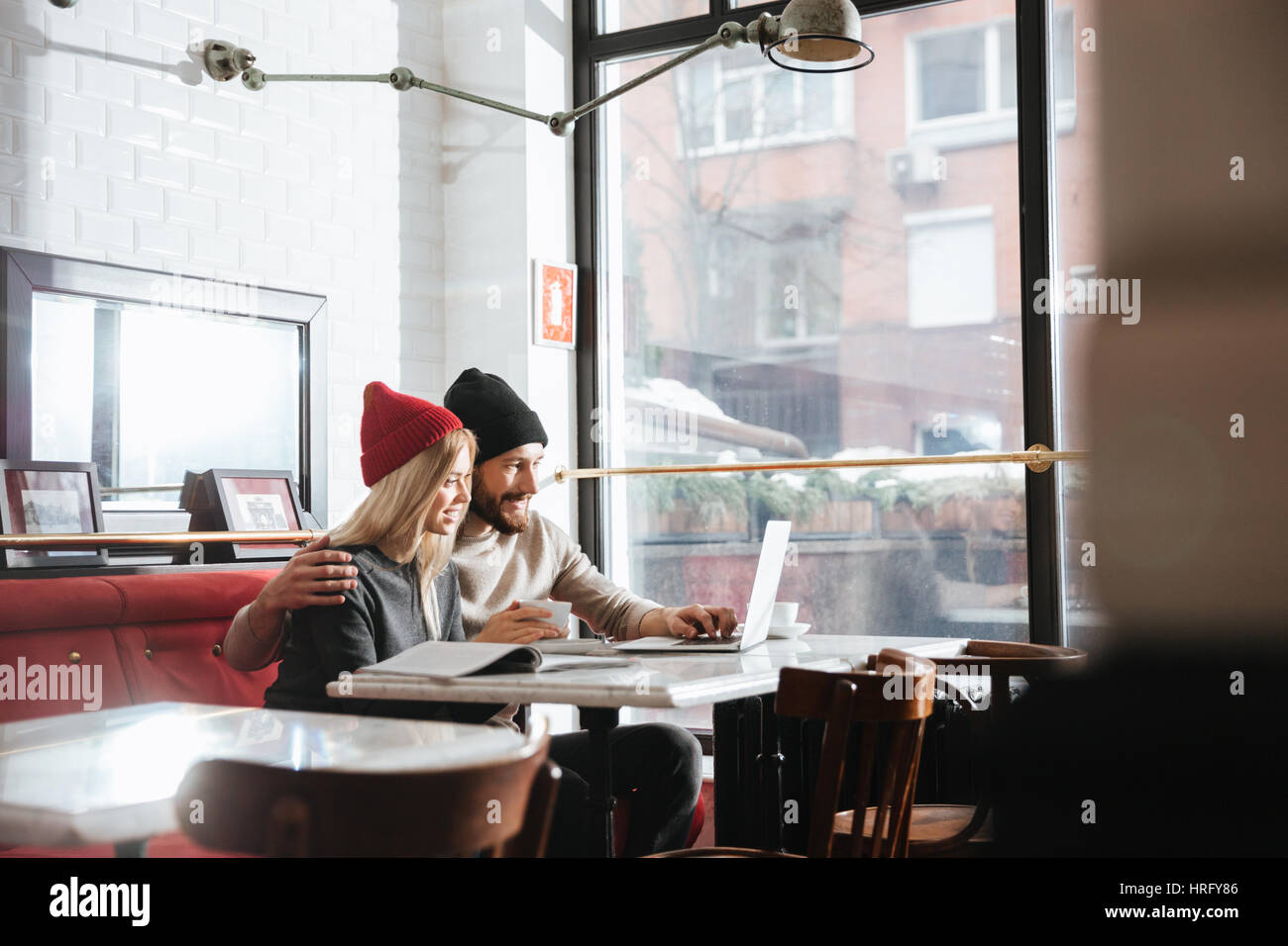Side view of young hipsters sitting by the table in cafe with laptop computer Stock Photo