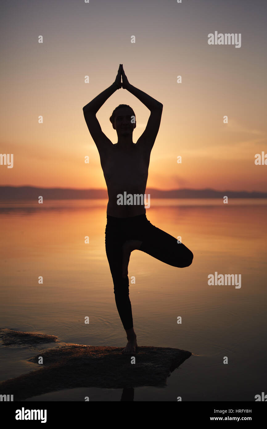 Silhouette of man practicing yoga pose on beach, standing on one leg
