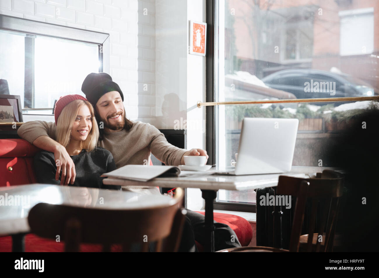 Side view of smiling hipsters sitting in cafe and looking at laptop Stock Photo