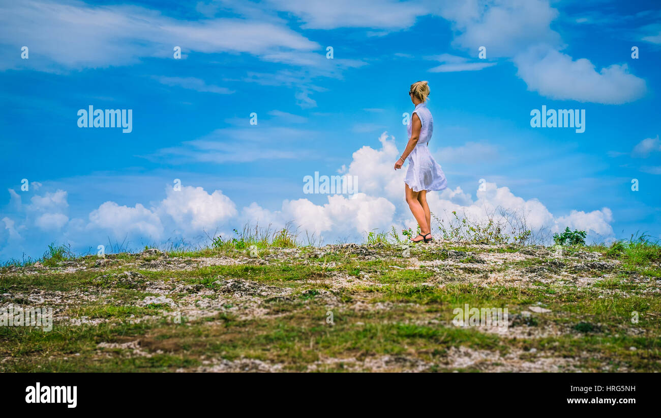A girl standing on Hill and looking at the white clouds, Teletubbies Hills, Nusa Penida, Bali, Indonesia Stock Photo