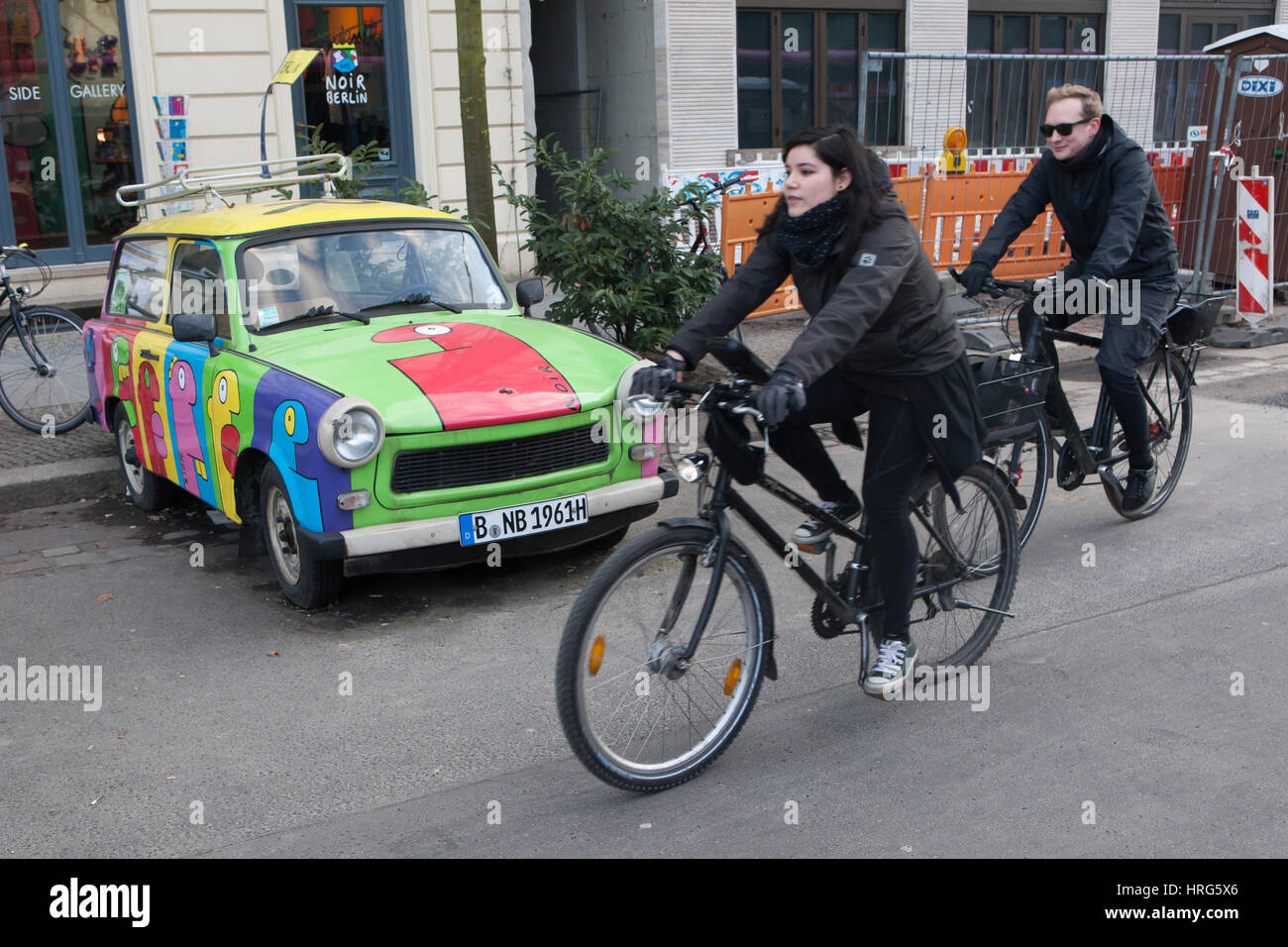 Cyclists pass by the Trabant painted by French artist Thierry Noir in Berlin, Germany. Stock Photo