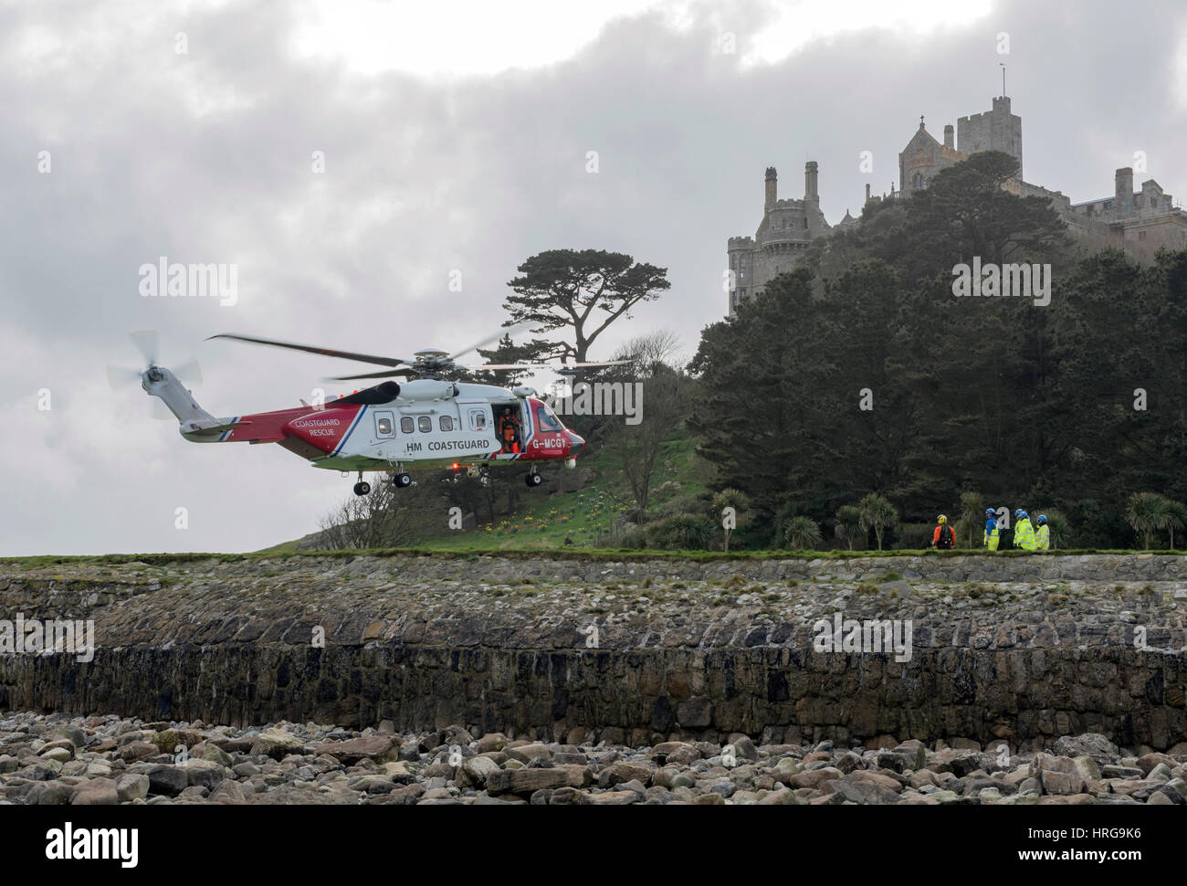 St Michaels Mount, Cornwall, UK. 1st March 2017. Newquay based coastguard Helicopter on approach to land, coastguard and one of the aircrew observe from the ground at St Michaels Mount, Cornwall,UK Credit: Bob Sharples/Alamy Live News Stock Photo