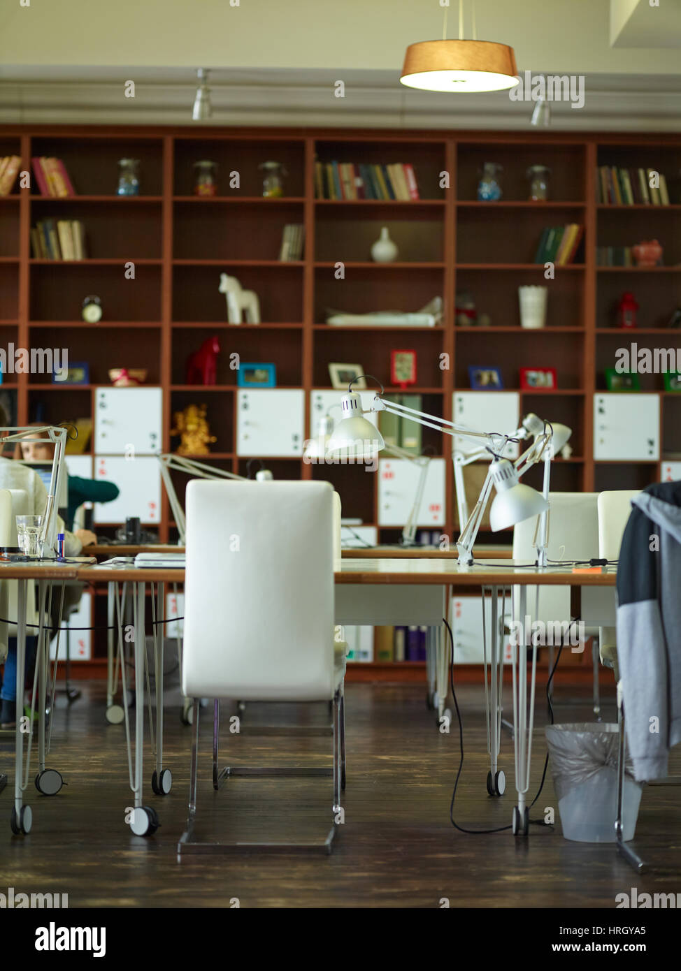 Working Desks With Lamps Against Tall Bookcases In Modern Office