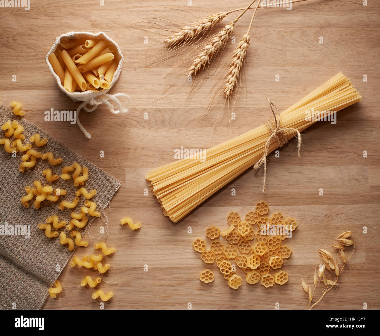 Top view of several types of dry pasta and wheat ears on light wooden table Stock Photo