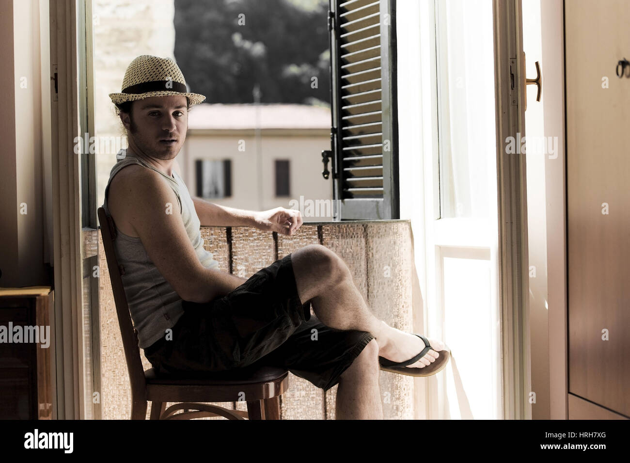 Model released, Junger Mann mit Hut sitzt am offenen Fenster - man with hat next to the window Stock Photo
