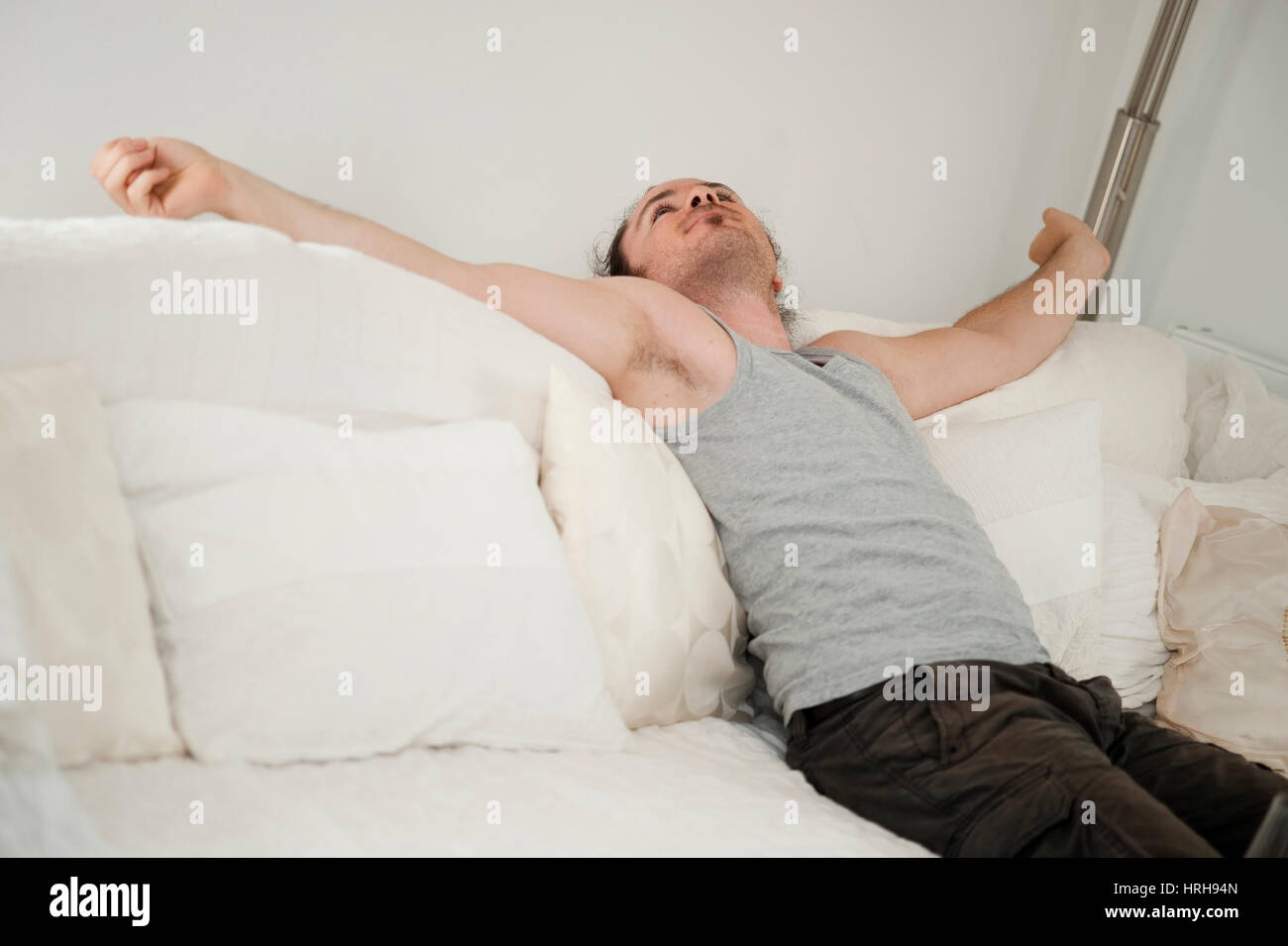 Model released, Junger Mann sitzt auf Couch und streckt sich - man relaxing on a couch Stock Photo