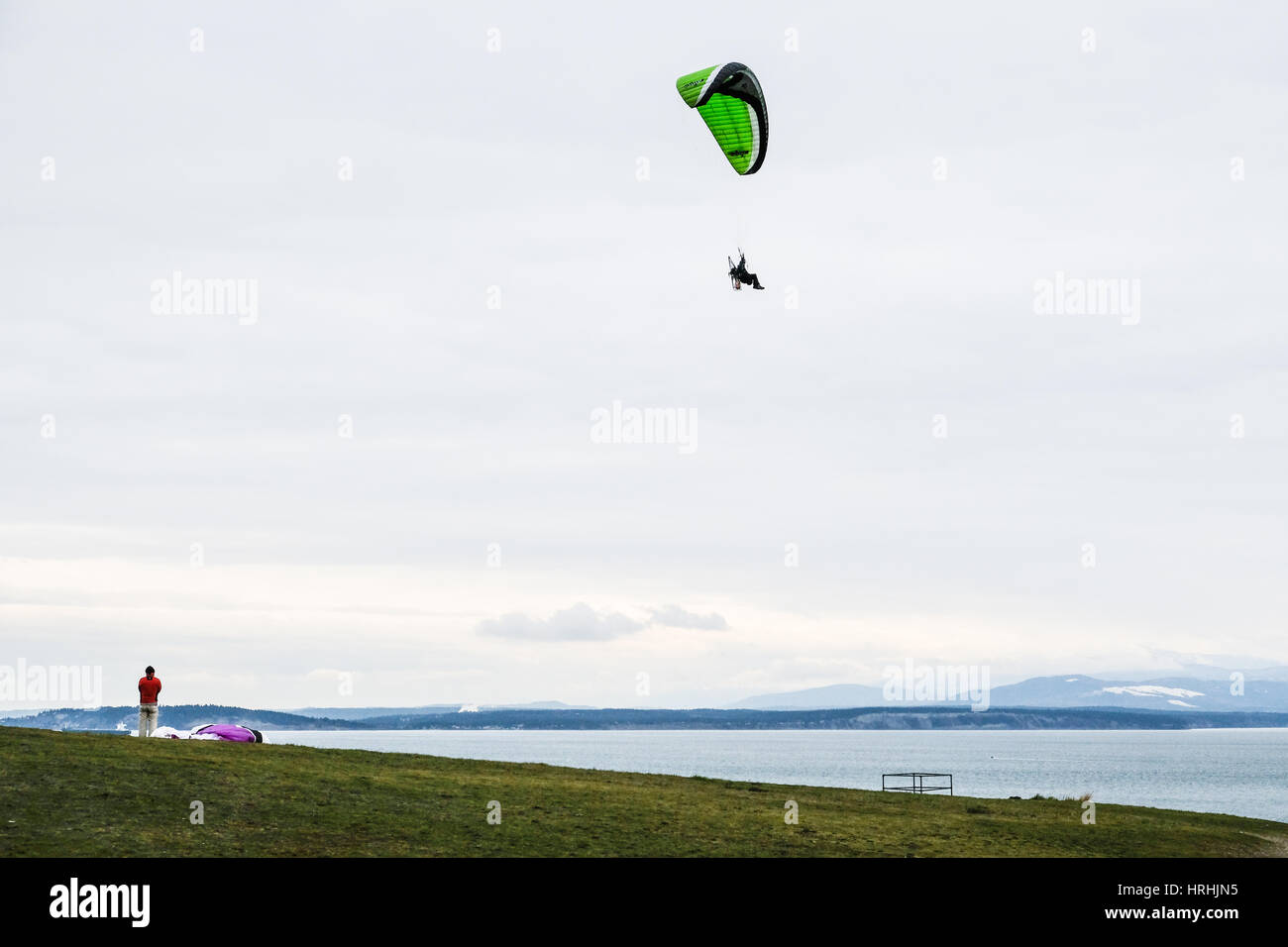 A Lone Moter Glider in the Sky Above Sea with People Watching Stock Photo