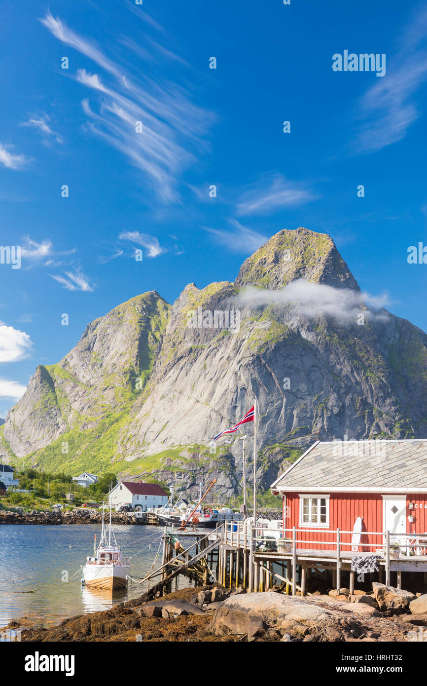 Typical house of fishermen called Rorbu framed by rocky peaks and blue sea, Reine, Moskenesoya, Lofoten Islands, Norway Stock Photo
