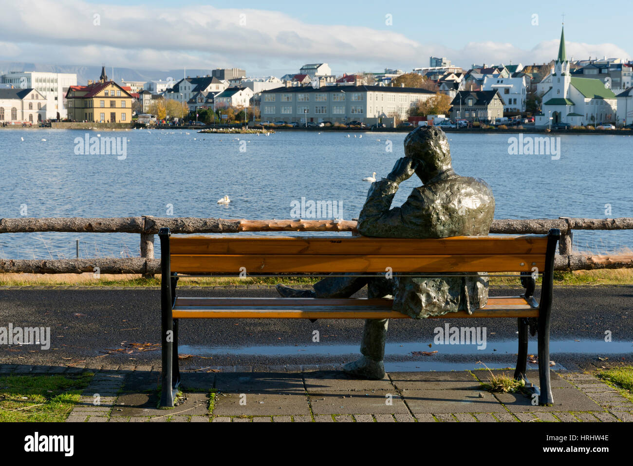 Sculpture of a man sitting on a park bench in front of Tjornin Lake and the Historic Centre of Rykjavik, Iceland, Polar Regions Stock Photo