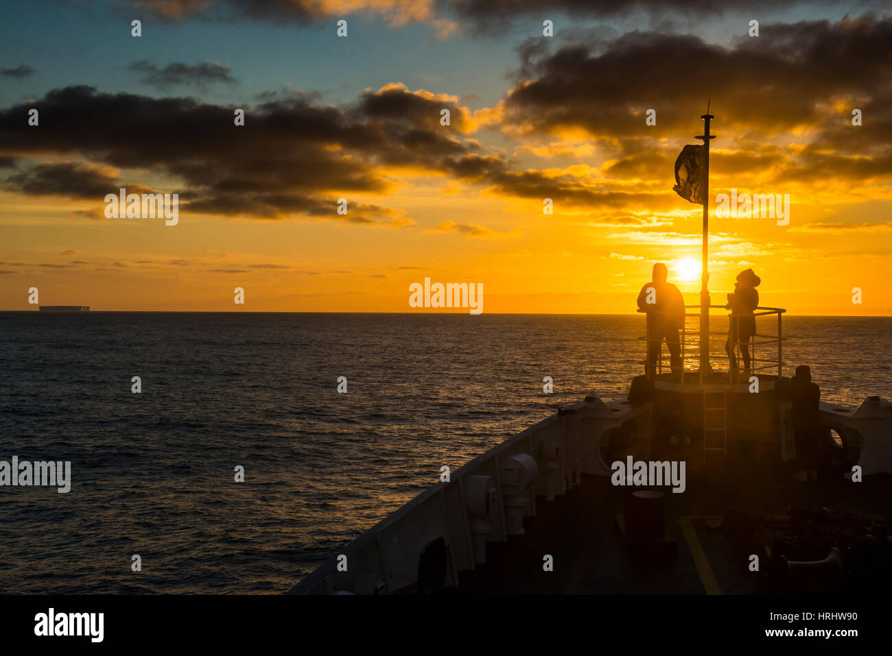 Tourists standing on the bow of a cruise ship watching the sunset ...