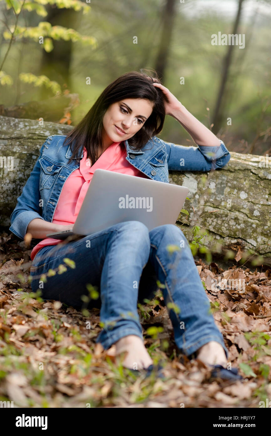 Junge Frau sitzt mit Laptop auf Laubboden im Wald - woman with laptop in nature Stock Photo