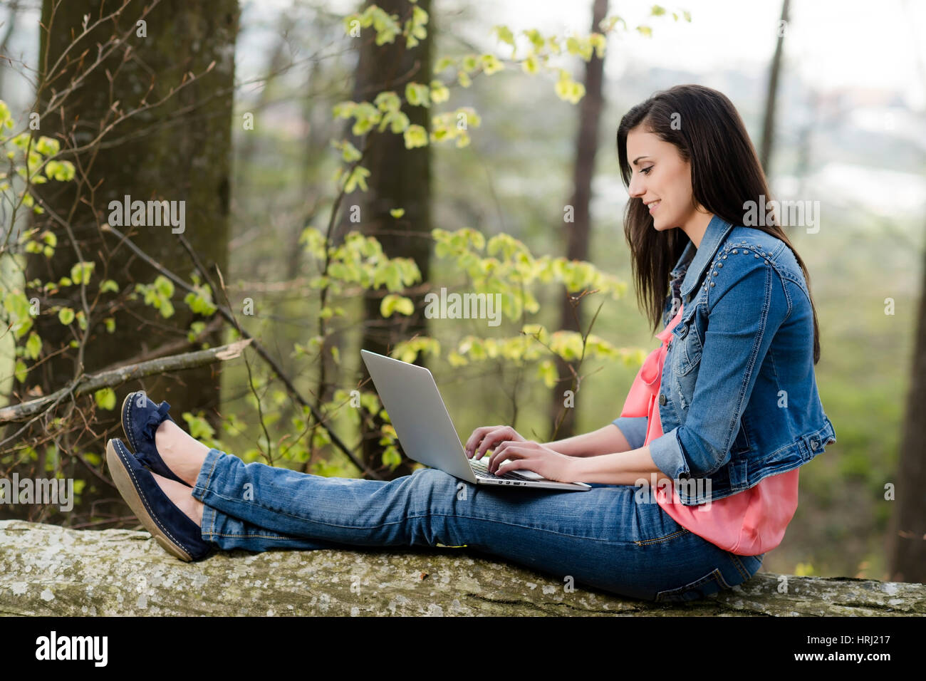 Junge Frau sitzt mit Laptop auf einem gefaellten Baumstamm - woman with laptop in nature Stock Photo